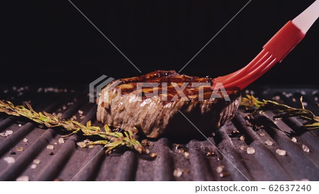 Delicious juicy meat steak cooking on grill. Prime rare roast grilling beef. Electric roaster, rosemary black pepper, salt. Silicone cooking brush. 62637240