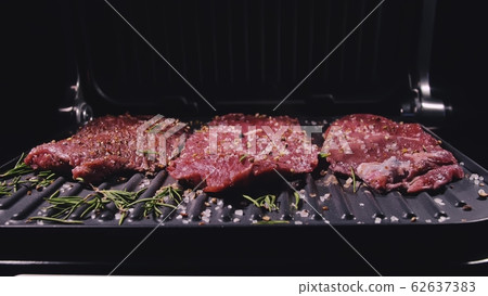 Delicious juicy meat steak cooking on grill. Prime beef fry on electric roaster, rosemary, black pepper, salt. Slow motion. 62637383