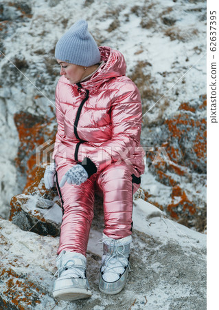 Woman is sitting in hill. Traveler is walking in top mountain. Beautiful girl is dressed in stylish pink down jacket. Magic purest place in nature. 62637395