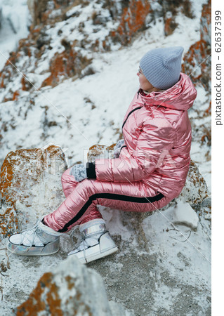 Woman is sitting in hill. Traveler is walking in top mountain. Beautiful girl is dressed in stylish pink down jacket. Magic purest place in nature. Woman is sitting in hill. Traveler is walking in top mountain. Beautiful girl is dressed in stylish pink down jacket. Magic purest place in nature. 62637399