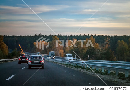 Autumn evening highway-highway along which cars and truck wagons ride along yellow trees Autumn evening highway-highway along which cars and truck wagons ride along yellow trees 62637672