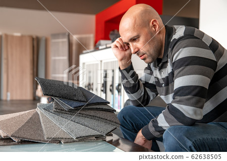 the man chooses the color of the new carpet according to the pattern book in the flooring shop 62638505