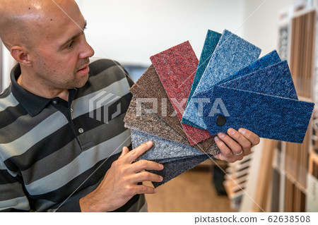 the man chooses the color of the new carpet according to the pattern book in the flooring shop the man chooses the color of the new carpet according to the pattern book in the flooring shop 62638508