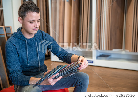 the man chooses the color of the new carpet according to the pattern book in the flooring shop the man chooses the color of the new carpet according to the pattern book in the flooring shop 62638530