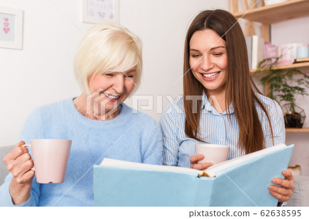 Grandmother and granddaughter watching old family album and laughing Grandmother and granddaughter watching old family album and laughing 62638595