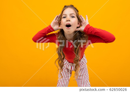 teenager girl with curly hair in a red blouse and striped trousers listens to the sounds on an teenager girl with curly hair in a red blouse and striped trousers listens to the sounds on an 62650026