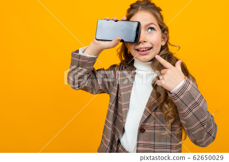 cute blonde girl in a classic jacket shows a phone with a mockup on a yellow background with copy 62650029