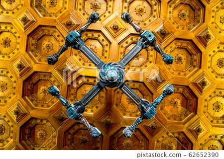 Beautiful carved wooden dark chandelier on a wooden patterned ceiling in an old manor Beautiful carved wooden dark chandelier on a wooden patterned ceiling in an old manor 62652390