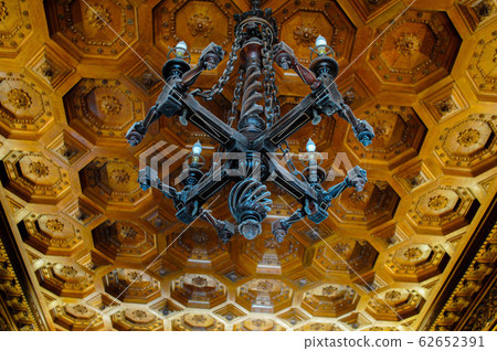 Beautiful carved wooden dark chandelier on a wooden patterned ceiling in an old manor Beautiful carved wooden dark chandelier on a wooden patterned ceiling in an old manor 62652391
