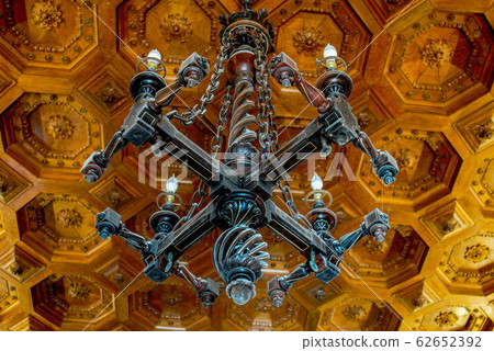 Beautiful carved wooden dark chandelier on a wooden patterned ceiling in an old manor Beautiful carved wooden dark chandelier on a wooden patterned ceiling in an old manor 62652392