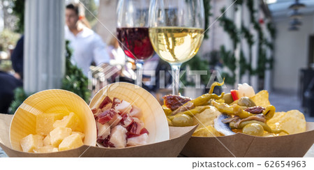 Tapas bar panorama. Cheese, ham and pinchos with peppers, with red and white wine in an outdoors cafe 62654963