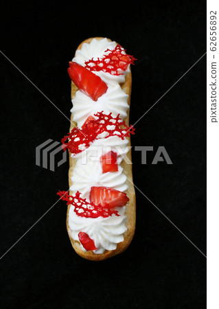 Strawberries and cream eclair with fresh berries and red lace tuile top down on black background Strawberries and cream eclair with fresh berries and red lace tuile top down on black background 62656892