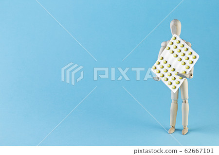 Wooden toy figure with pills on blue background. Wooden toy figure with pills on blue background. 62667101