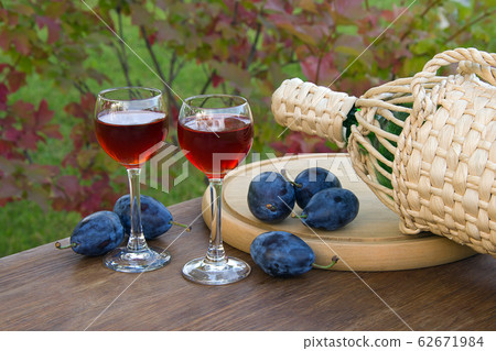 Plum alcoholic drink in two glass glasses and bottle with ripe plums in a wooden plate on a natural background 62671984