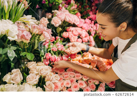 Smiling woman looking on flowers in her shop. Female florist choosing flowers for a bouquet. Smiling woman looking on flowers in her shop. Female florist choosing flowers for a bouquet. 62672614