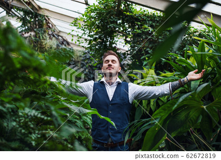 Young man standing in botanical garden, arms stretched. Young man standing in botanical garden, arms stretched. 62672819