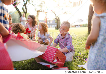 Down syndrome child with friends on birthday party outdoors, opening presents. 62672832