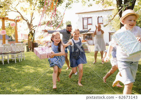 Small children ruunning with present outdoors in garden on birthday party. Small children ruunning with present outdoors in garden on birthday party. 62673143