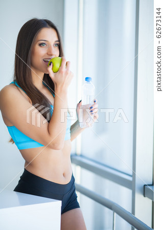 Beautiful fit young woman holding a bottle of water and green apple 62673144