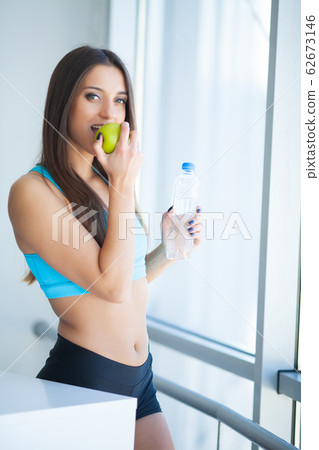 Beautiful fit young woman holding a bottle of water and green apple 62673146