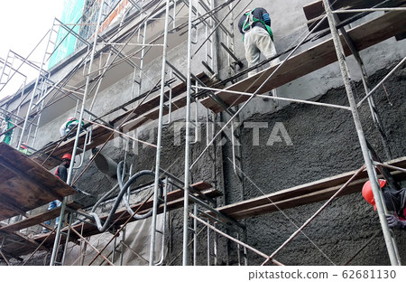 Brick wall plastered by construction workers using the cement plaster. Scaffolding used as temporary staging to work at height. Wearing appropriate safety gear to prevent bad happen.   62681130