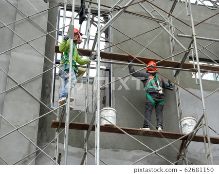 Brick wall plastered by construction workers using the cement plaster. Scaffolding used as temporary staging to work at height. Wearing appropriate safety gear to prevent bad happen.   62681150