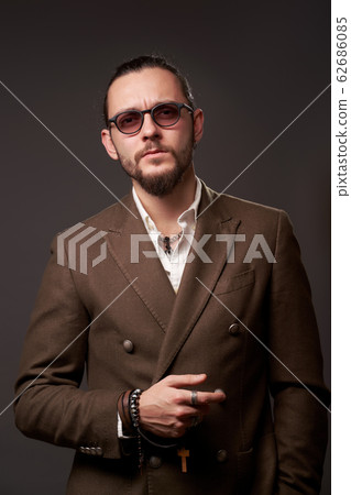 Serious man with beard in jacket looks at camera on empty brown background 62686085
