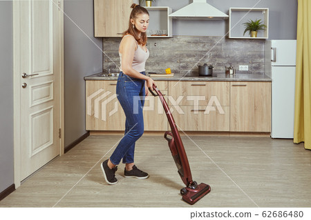 One young woman uses a wireless vacuum cleaner. One young woman uses a wireless vacuum cleaner. 62686480