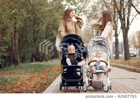 Two young mothers walking in a autumn park with carriages 62687703