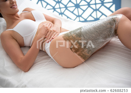 Pretty female on mud wrapping procedure of legs Pretty female on mud wrapping procedure of legs 62688253
