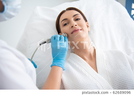 Young lady having face roll massage procedure Young lady having face roll massage procedure 62689096