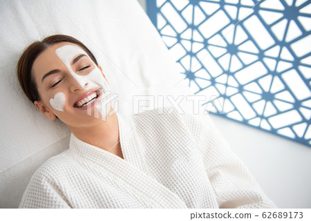 Pretty smiling lady laying on couch with face mask Pretty smiling lady laying on couch with face mask 62689173