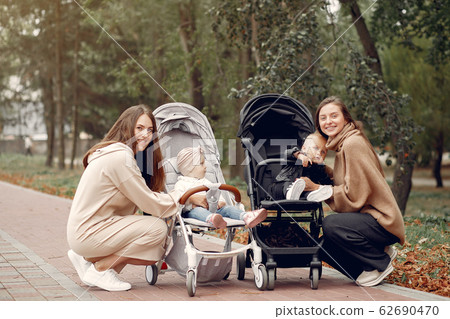 Two young mothers walking in a autumn park with carriages Two young mothers walking in a autumn park with carriages 62690470