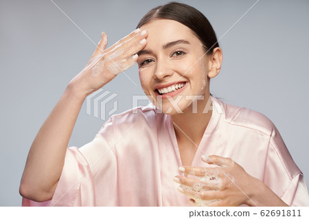 Joyful pretty girl washing face with foaming cleanser 62691811