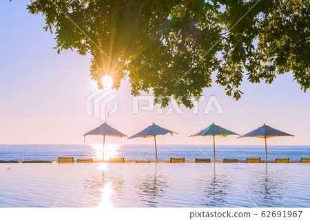 Beautiful tropical outdoor beach sea ocean with umbrella and chiar around outdoor swimming pool at sunset or sunrise time 62691967