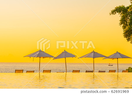 Beautiful tropical outdoor beach sea ocean with umbrella and chiar around outdoor swimming pool at sunset or sunrise time 62691969