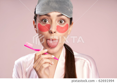Charming young woman with under-eyes patches showing her tongue Charming young woman with under-eyes patches showing her tongue 62691994