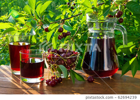 Fresh cherry juice in a decanter and glasses with ripe cherries on a wooden table in the garden Fresh cherry juice in a decanter and glasses with ripe cherries on a wooden table in the garden 62694239
