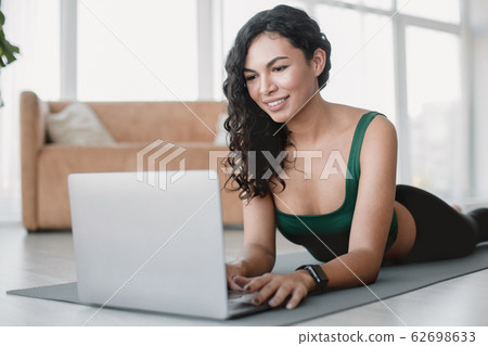 Smiling Hispanic woman with laptop on yoga mat indoors 62698633