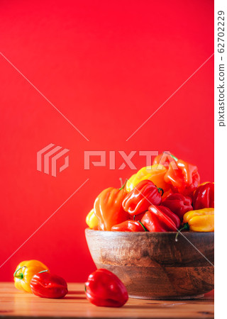 Yellow and red scotch bonnet chili peppers in wooden bowl over red background. Copy space. Yellow and red scotch bonnet chili peppers in wooden bowl over red background. Copy space. 62702229