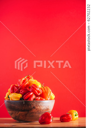 Colorful scotch bonnet chili peppers in wooden bowl over red background. Copy space. Colorful scotch bonnet chili peppers in wooden bowl over red background. Copy space. 62702232