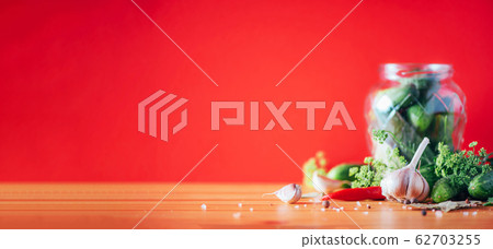 Pickling cucumbers in cans. Ingredients for marinated gherkins, glass jar, garlic, dill, salt, pepper on red background. Copy space. Concept of vegetables preservation. Pickling cucumbers in cans. Ingredients for marinated gherkins, glass jar, garlic, dill, salt, pepper on red background. Copy space. Concept of vegetables preservation. 62703255