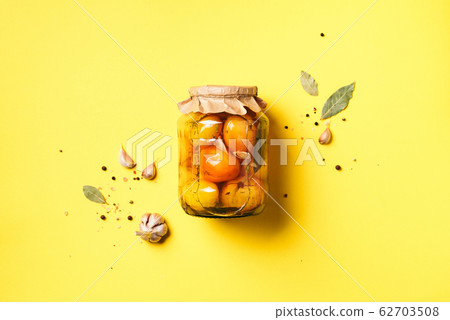 Pickled tomatoes in jar on yellow background. Top view. Flat lay. Copy space. Canned and preserved vegetables. Ingredients for vegetables preserving. Healthy fermented food concept. 62703508