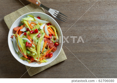 top view of spicy mango salad in a ceramic bowl on wooden table. 62706080