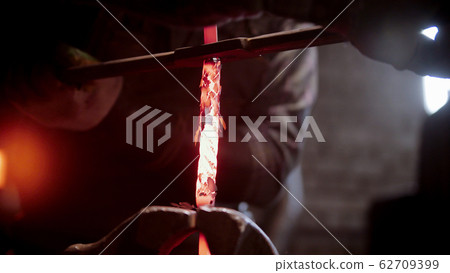 A blacksmith twisting a hot piece of metal in clamps 62709399
