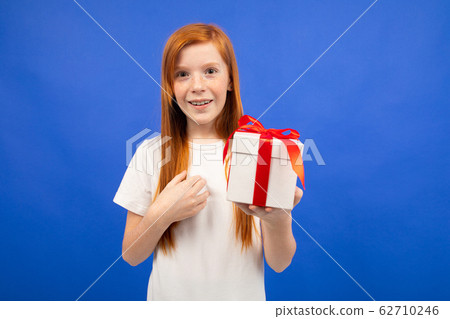 happy joyful teenager girl with red hair does not believe happiness holding a gift box on a blue happy joyful teenager girl with red hair does not believe happiness holding a gift box on a blue 62710246