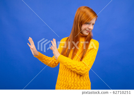 offended european red-haired teenager girl in a yellow sweater waved her hands in denial on a blue offended european red-haired teenager girl in a yellow sweater waved her hands in denial on a blue 62710251
