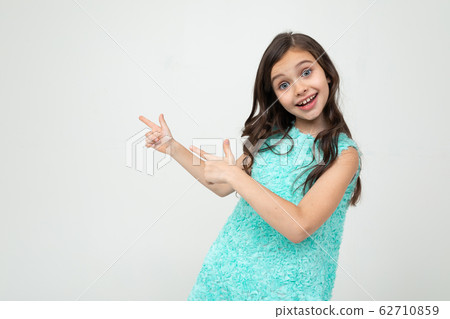 smiling teenage girl in a blue dress points her hands towards empty space on a white studio 62710859