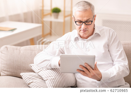 Elderly man using digital tablet sitting on sofa Elderly man using digital tablet sitting on sofa 62710985