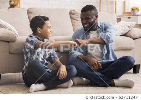 Cheerful Black Preteen Boy Fist Bumping With His Dad At Home Cheerful Black Preteen Boy Fist Bumping With His Dad At Home 62711247